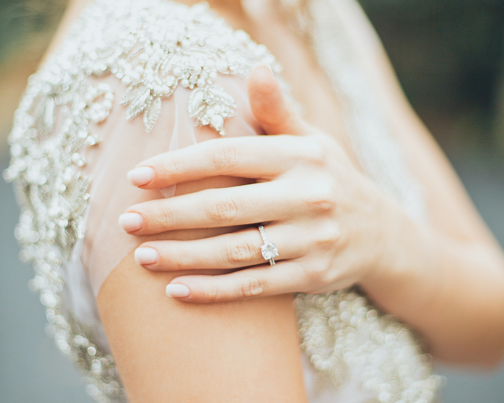 Woman in wedding gown holding her shoulder to present engagement ring