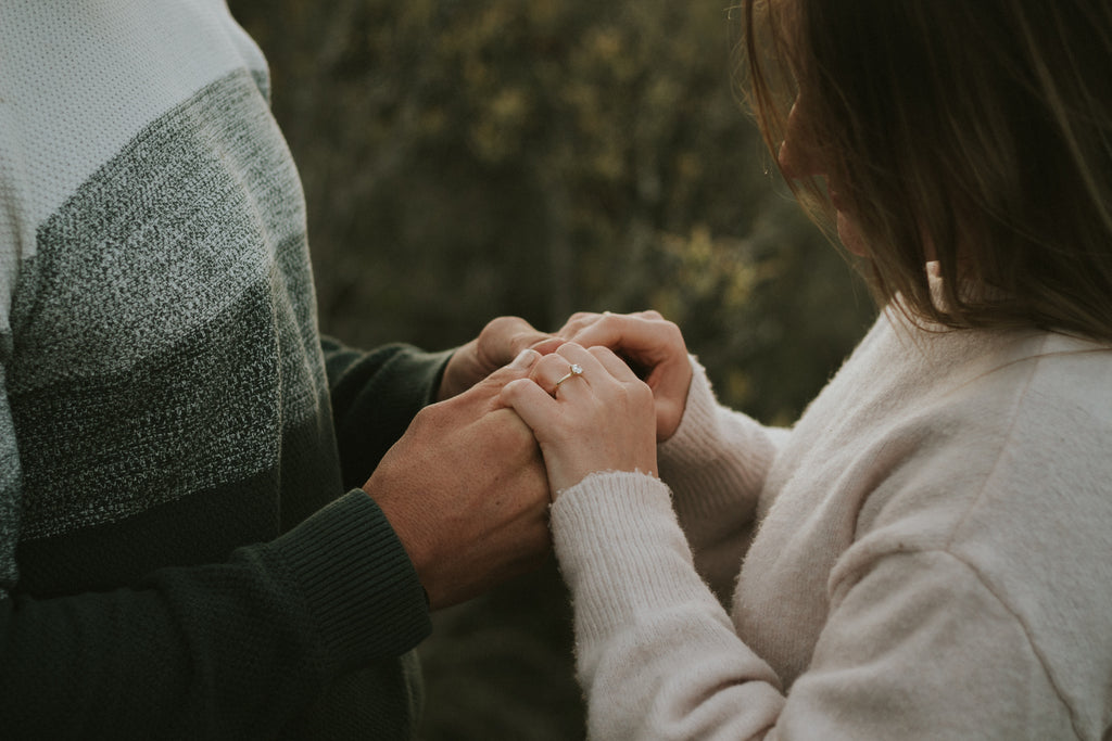 moody-tone-couple-holding-hands-looking-at-engagement-ring-on-womans-finger