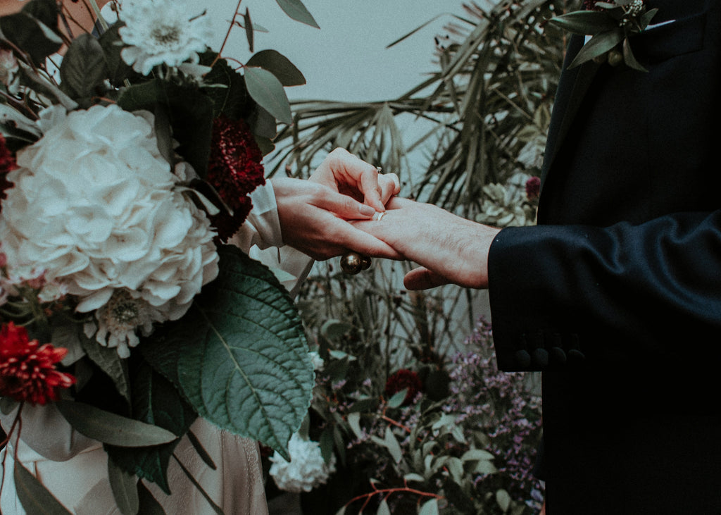 Woman with bouquet placing wedding ring on man's finger